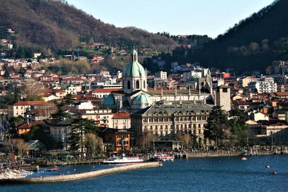 Lake Como waterfront with boats and Como Cathedral below wooded hills