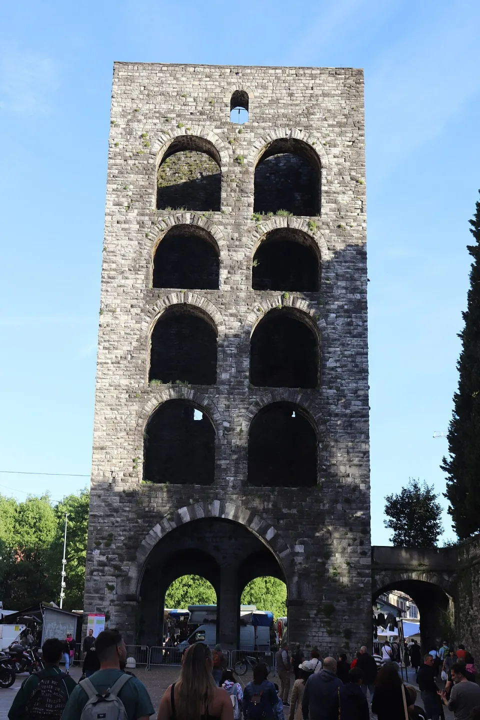 Stone arches of Porta Torre in Como under a blue sky, with pedestrians below