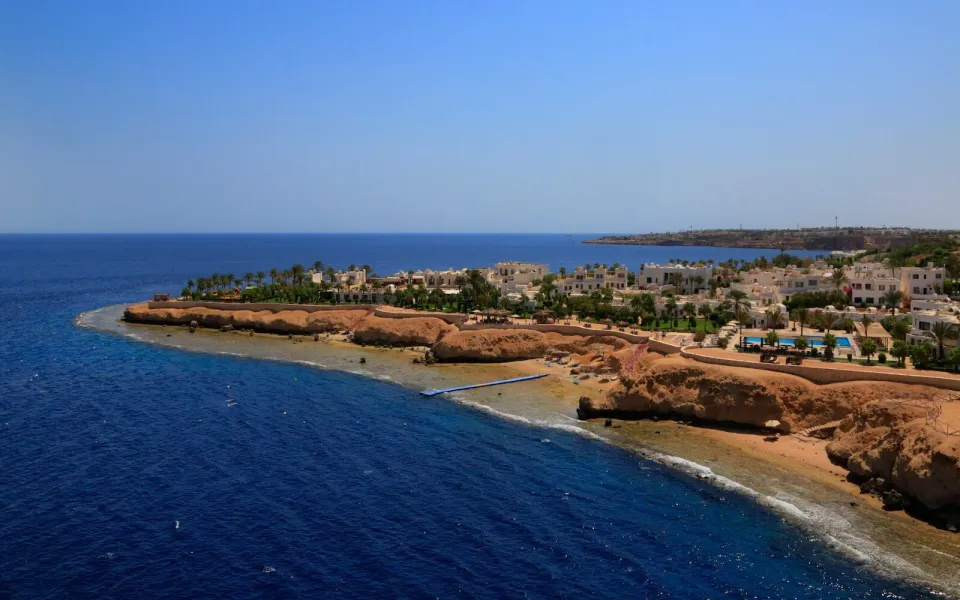 海から見たSharm Clubの白い村と低い崖。浅い珊瑚の棚を越える細い青い桟橋が見える