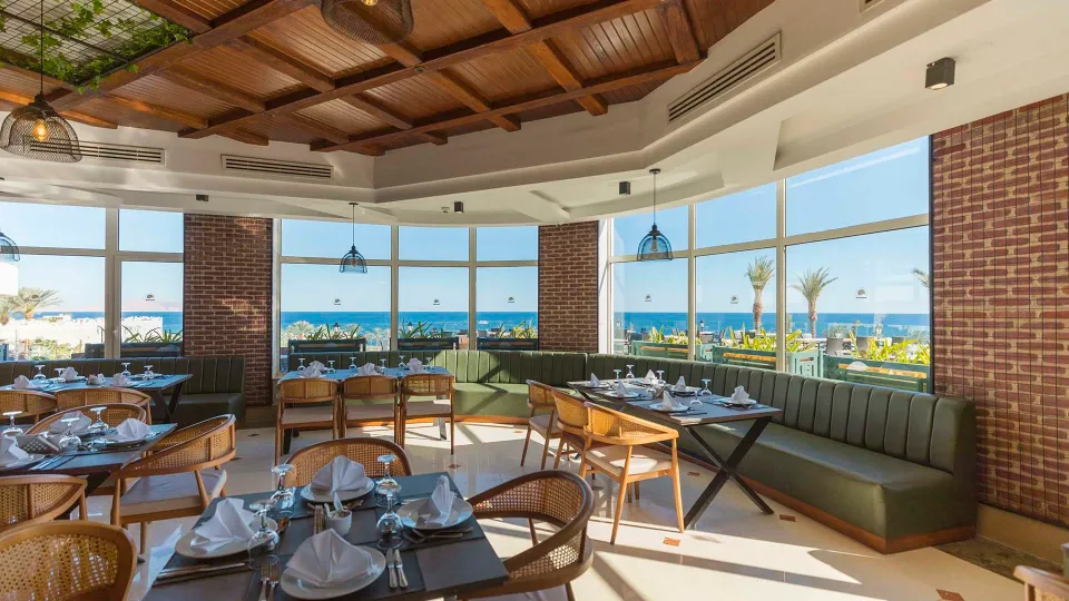 Diamond BeachのBasilico Restaurant。緑のソファ席と籐の椅子、窓の向こうの海
