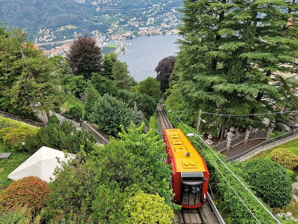 Red and yellow Como–Brunate funicular descending through trees with Lake Como behind it
