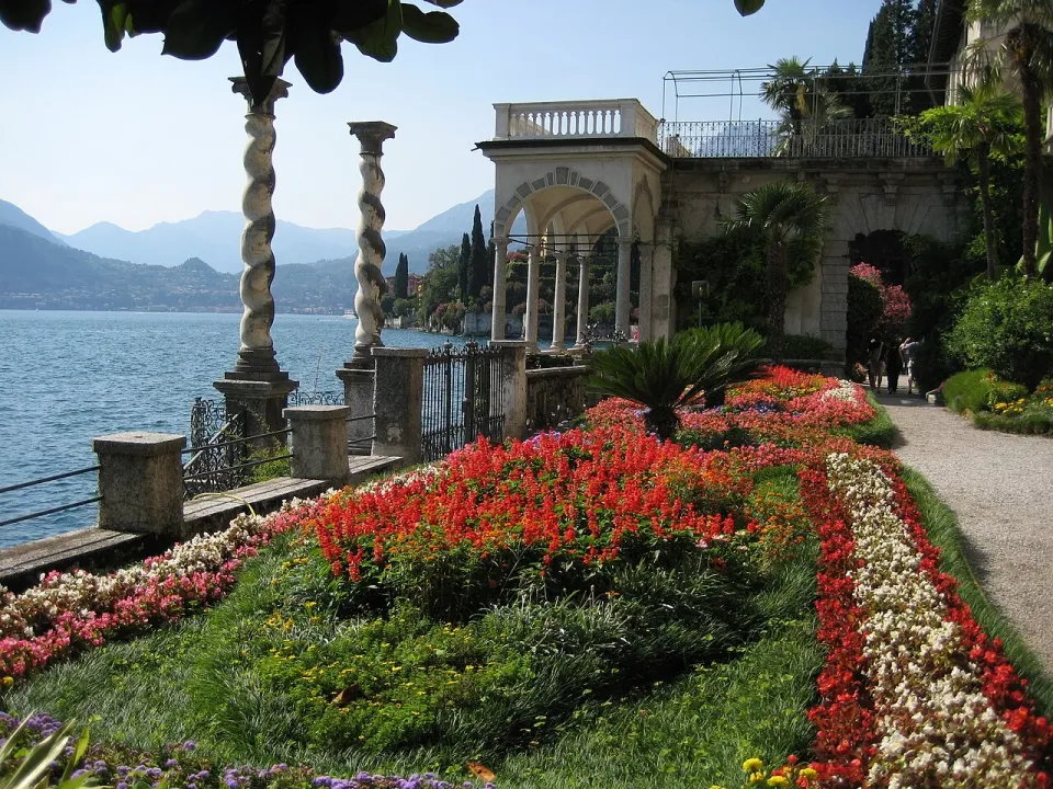 Red and white flower beds, twisted columns and an arched terrace beside Lake Como in Villa Monastero’s garden