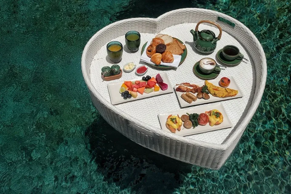ロイヤルプルナマのハート形の白いトレーに並ぶ卵料理、パン、果物と飲み物。