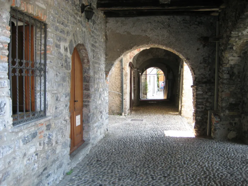 Cobblestone passage with stone arches, wooden doors and bright daylight at the far end in Varenna