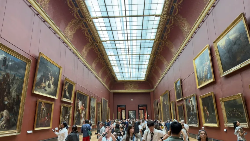 赤い壁に大型の絵画が並び多くの来館者でにぎわうルーブル美術館の展示室