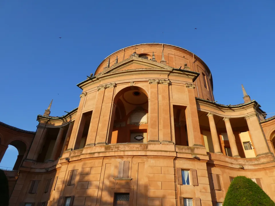 The curved orange façade and columns of the Madonna di San Luca sanctuary beneath a blue sky