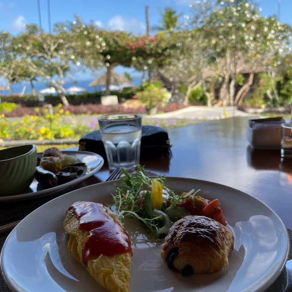 庭と海を望む席に置かれた朝食の卵料理とパン