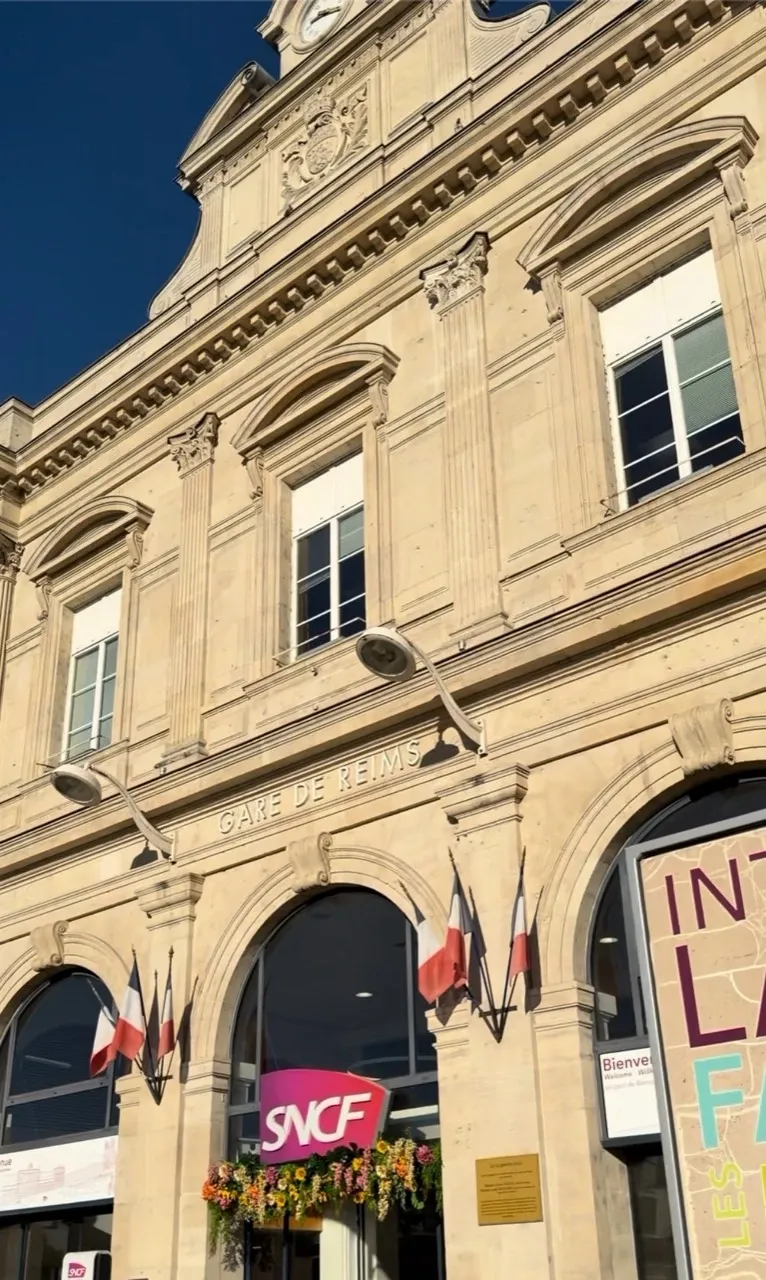 GARE DE REIMSの文字とフランス国旗が見えるランス駅の石造りの駅舎