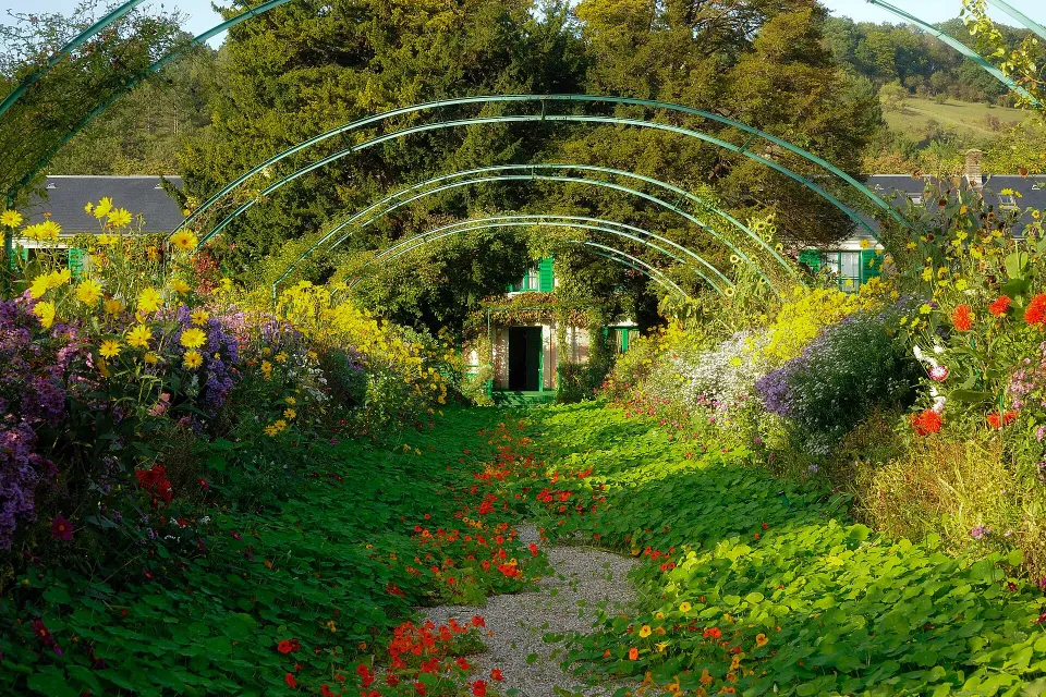ジヴェルニーのモネの庭で、緑のアーチが連なる通路に赤や黄色、紫の花が咲く