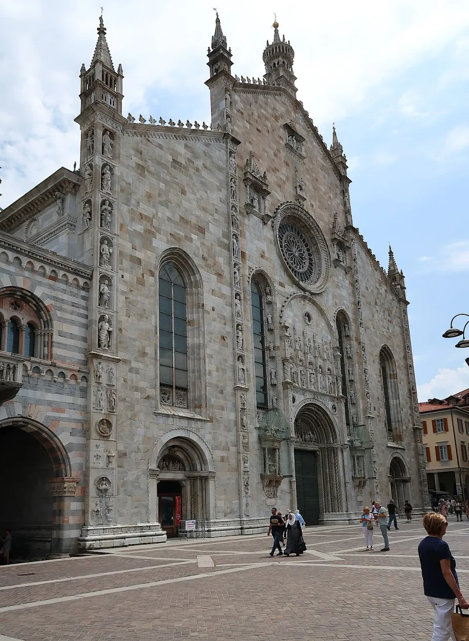 Rose window, statues and spires on the west facade of Como Cathedral, seen from the square
