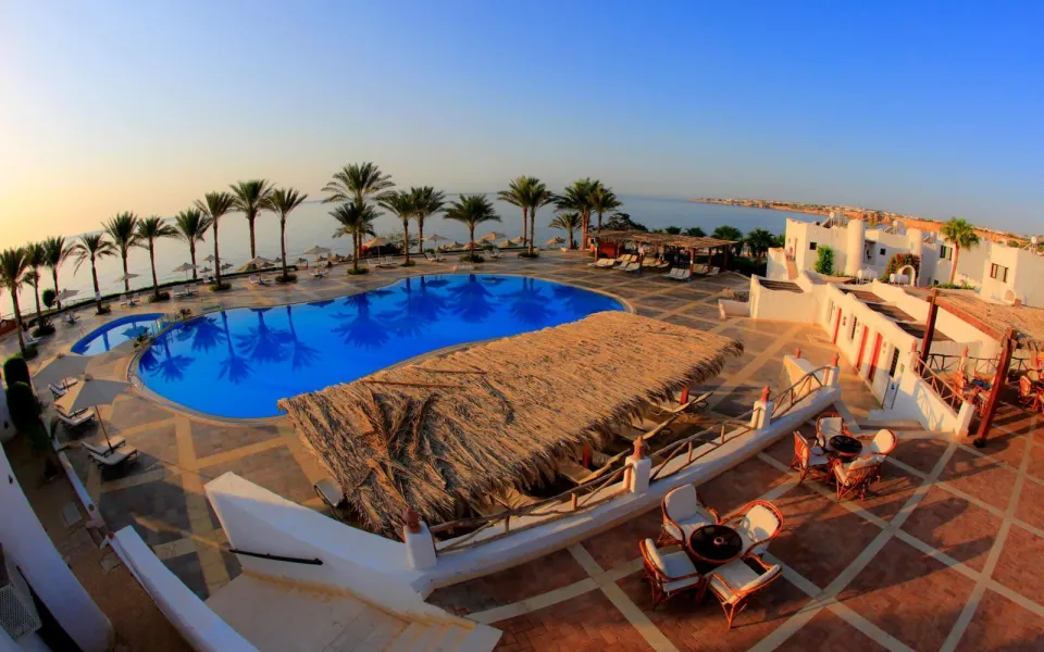 Sharm Clubの曲線プールとヤシ、低い白い建物。テラスの先には紅海の水平線が広がる